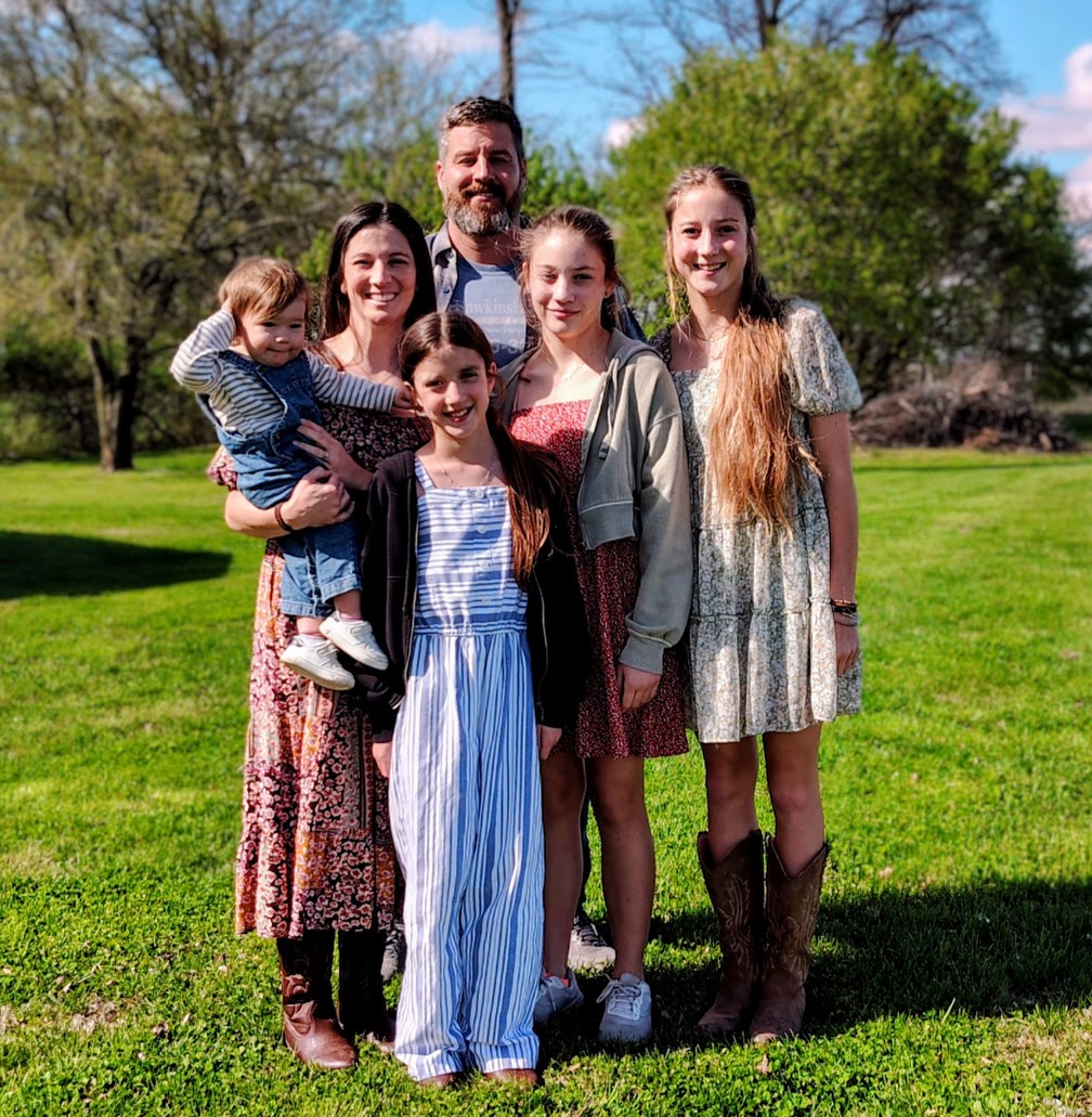 The Miller family standing together on a sunlit lawn — Jared and Amber with their four children Kiah, Zoe, Phoebe, and Derek.